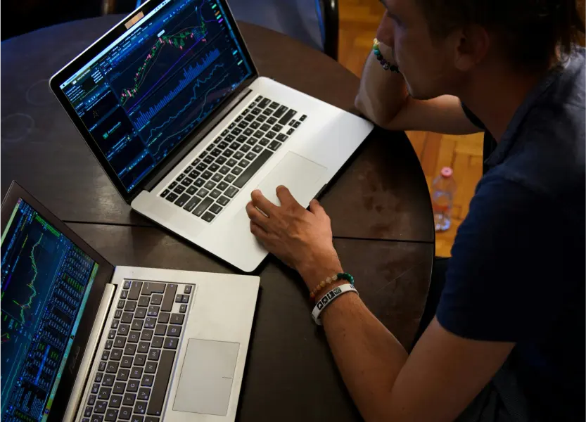 An analyst reviewing market charts across two laptops
